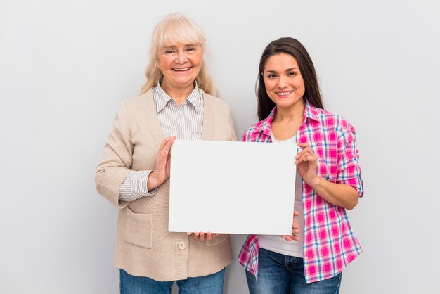 Retrato de mujer senior y su hija mostrando un cartel blanco en blanco