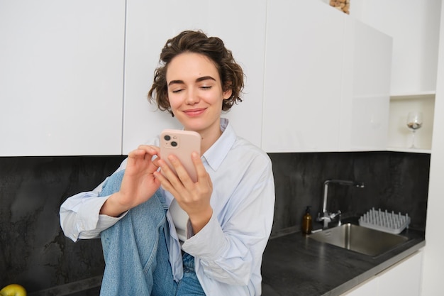 Foto gratuita retrato de una mujer sentada en casa con un teléfono móvil comprando en línea en una aplicación para teléfonos inteligentes pasando tiempo