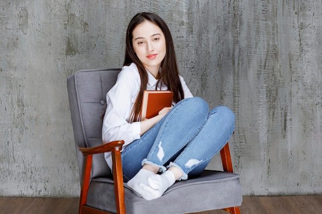 Retrato de mujer sentada en un sillón con un libro posando. foto de alta calidad
