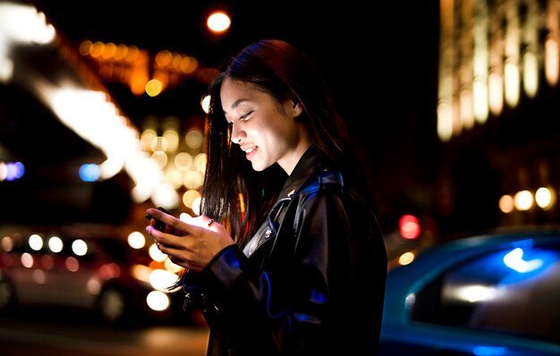 Retrato de mujer con smartphone por la noche en las luces de la ciudad