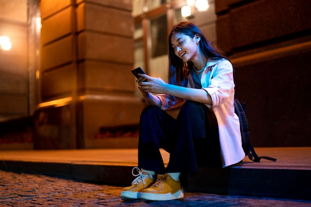 Foto gratuita retrato de mujer con smartphone por la noche en las luces de la ciudad