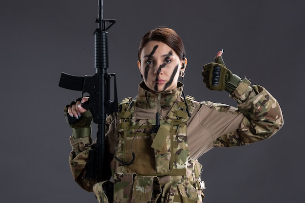 Retrato de mujer soldado en camuflaje con ametralladora en la pared oscura