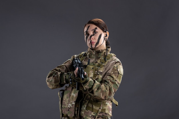 Retrato de mujer soldado en camuflaje con ametralladora en la pared oscura