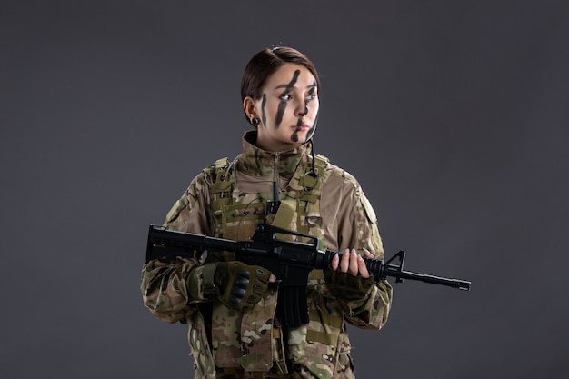 Retrato de mujer soldado en camuflaje con ametralladora en la pared oscura