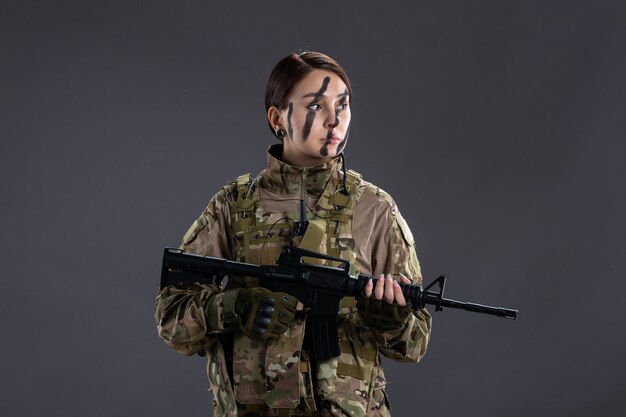 Retrato de mujer soldado en camuflaje con ametralladora en la pared oscura