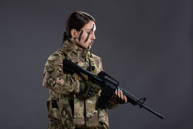 Retrato de mujer soldado en camuflaje con ametralladora en la pared oscura