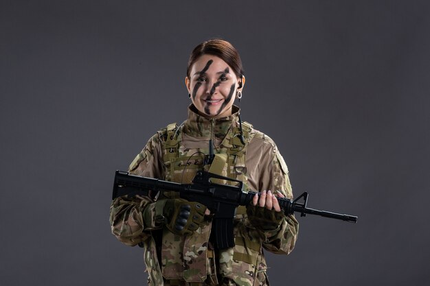 Retrato de mujer soldado en camuflaje con ametralladora en la pared oscura