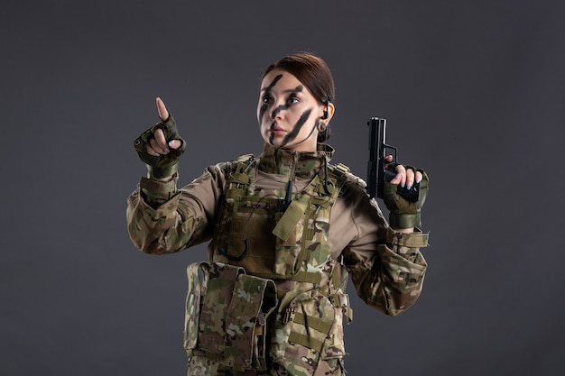 Retrato de mujer soldado en camuflaje con pistola pared oscura