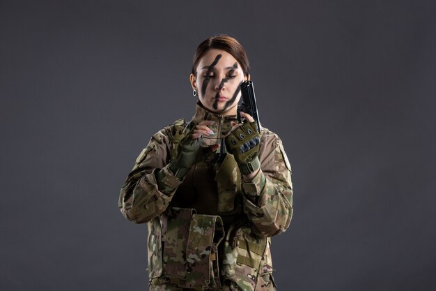 Retrato de mujer soldado en camuflaje con pistola pared oscura