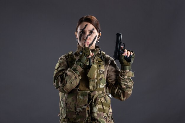 Retrato de mujer soldado en camuflaje con pistola pared oscura