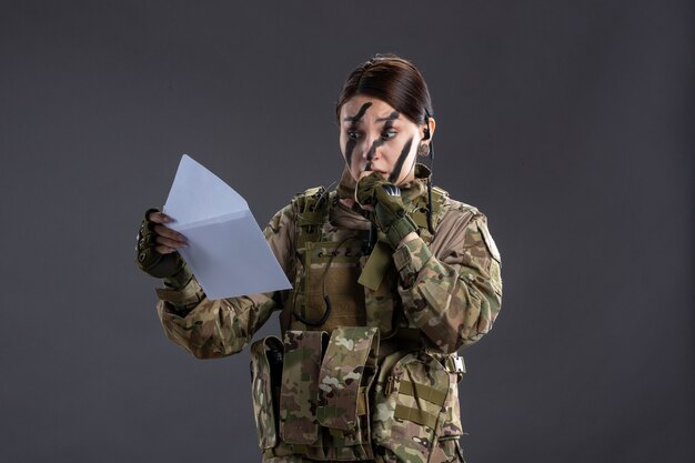 Retrato de mujer soldado leyendo carta en la pared oscura