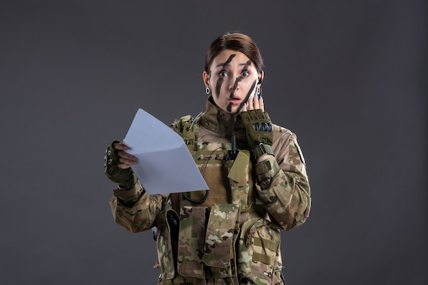 Retrato de mujer soldado leyendo carta en la pared oscura