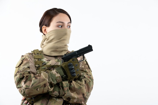 Retrato de mujer soldado con pistola en pared blanca de camuflaje