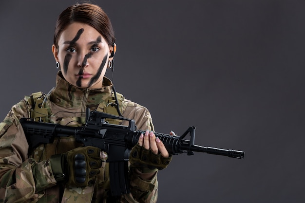 Retrato de mujer soldado en uniforme militar con ametralladora en la pared oscura