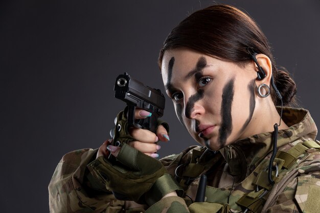 Retrato de mujer soldado en uniforme militar con pistola en la pared oscura