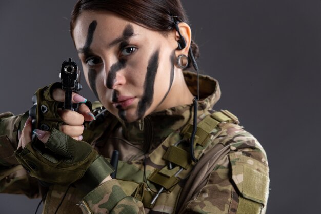 Retrato de mujer soldado en uniforme militar con pistola en la pared oscura