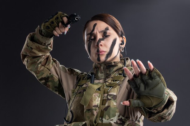 Retrato de mujer soldado en uniforme militar con pistola en la pared oscura