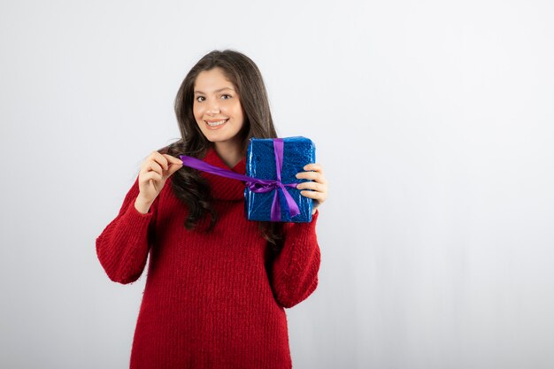 Retrato de una mujer sonriente abriendo una caja de regalo de Navidad con cinta morada.