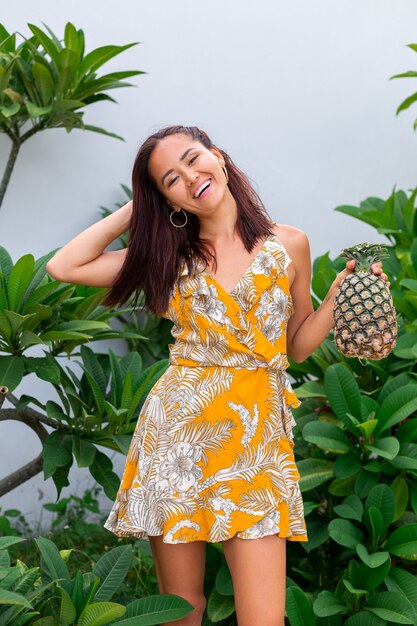 Retrato de mujer sonriente asiática feliz en vestido amarillo de verano mantenga piña