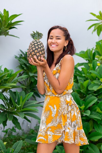 Retrato de mujer sonriente asiática feliz en vestido amarillo de verano mantenga piña