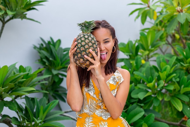 Retrato de mujer sonriente asiática feliz en vestido amarillo de verano mantenga piña