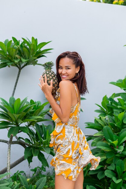 Retrato de mujer sonriente asiática feliz en vestido amarillo de verano mantenga piña