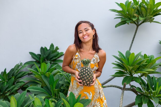 Retrato de mujer sonriente asiática feliz en vestido amarillo de verano mantenga piña