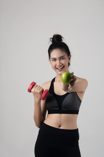 Retrato de mujer sonriente atractiva con manzana y pesas aisladas sobre fondo blanco.