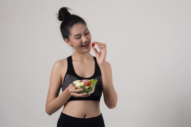 Retrato de la mujer sonriente atractiva que come la ensalada aislada en el fondo blanco.