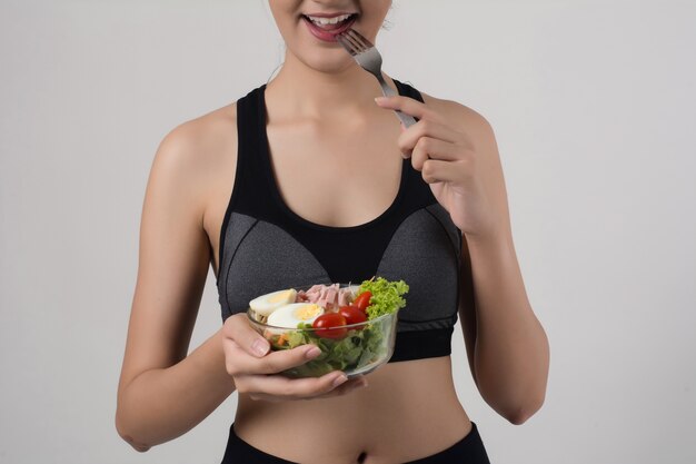Retrato de la mujer sonriente atractiva que come la ensalada aislada en el fondo blanco.