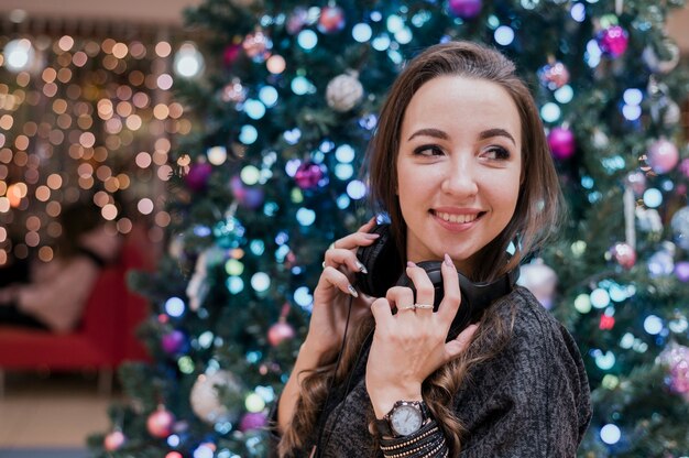 Retrato de mujer sonriente con auriculares cerca de árbol de Navidad mirando a otro lado