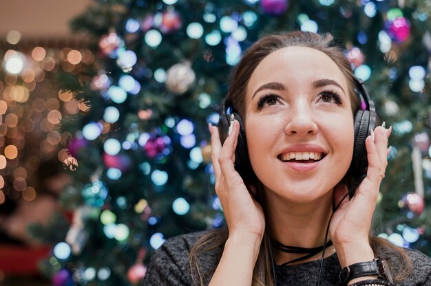 Retrato de mujer sonriente con auriculares cerca de árbol de Navidad