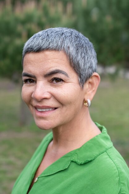 Retrato de mujer sonriente con cabello gris en el parque. Modelo femenino con cabello gris corto en ropa brillante mirando a la cámara. Belleza, concepto de retrato