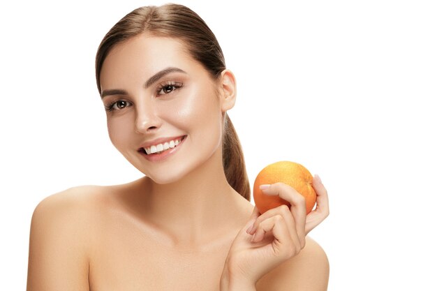 El retrato de mujer sonriente caucásica atractiva aislada en la pared blanca con fruta anaranjada. La belleza, cuidado, piel, tratamiento, salud, spa, cosmética