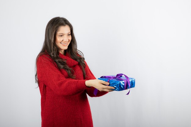 Retrato de una mujer sonriente dando una caja de regalo de Navidad con cinta morada.