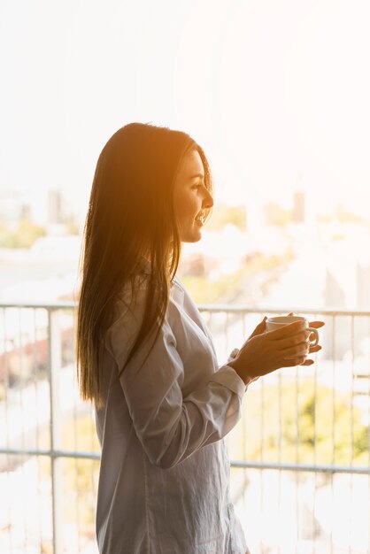 Retrato de una mujer sonriente disfrutando el café de la mañana en el balcón