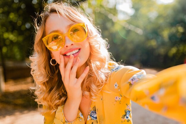 Foto gratuita retrato de mujer sonriente elegante rubia hermosa en blusa amarilla con gafas de sol haciendo foto selfie