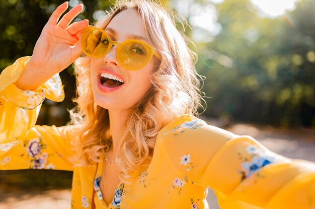 Retrato de mujer sonriente elegante rubia hermosa en blusa amarilla con gafas de sol haciendo foto selfie