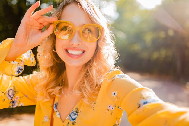 Retrato de mujer sonriente elegante rubia hermosa en blusa amarilla con gafas de sol haciendo foto selfie