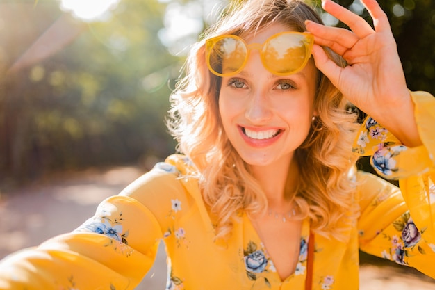 Retrato de mujer sonriente elegante rubia hermosa en blusa amarilla con gafas de sol haciendo foto selfie