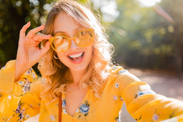 Foto gratuita retrato de mujer sonriente elegante rubia hermosa en blusa amarilla con gafas de sol haciendo foto selfie