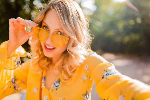 Retrato de mujer sonriente elegante rubia hermosa en blusa amarilla con gafas de sol haciendo foto selfie
