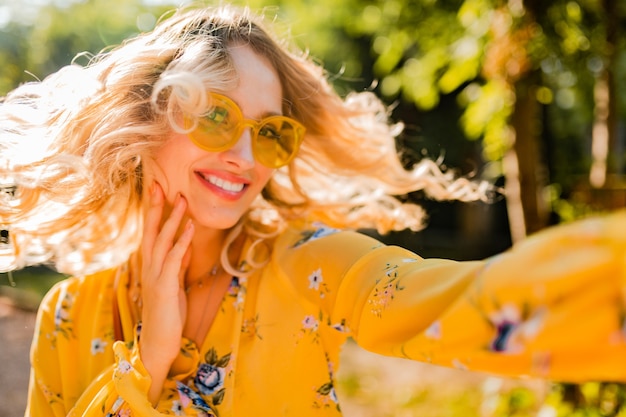 Retrato de mujer sonriente elegante rubia hermosa en blusa amarilla con gafas de sol haciendo foto selfie