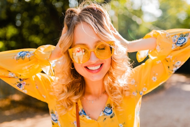 Retrato de mujer sonriente elegante rubia hermosa en blusa amarilla con gafas de sol