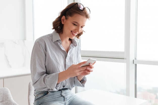 Foto gratuita retrato de una mujer sonriente enviando mensajes de texto en el teléfono móvil