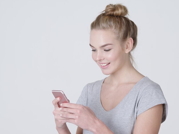 Retrato de una mujer sonriente está escribiendo un mensaje de texto en el teléfono móvil - en el estudio