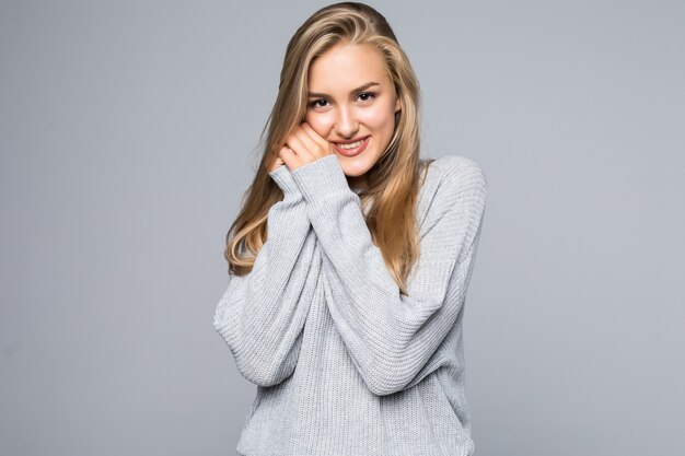 Retrato de una mujer sonriente feliz en suéter con las manos cerca de la cara mirando a otro lado aislado en el fondo gris