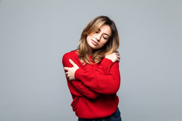 Retrato de una mujer sonriente feliz en suéter rojo con las manos cruzadas mirando a otro lado aislado en la pared gris