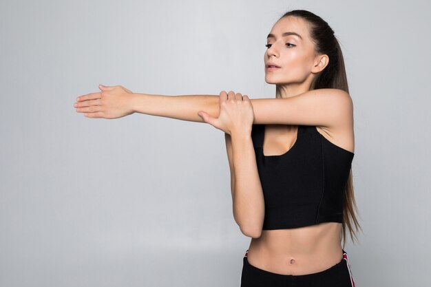 Retrato de una mujer sonriente de fitness estirando sus manos sobre la pared blanca