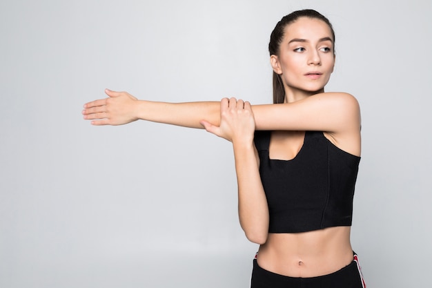 Retrato de una mujer sonriente de fitness estirando sus manos sobre la pared blanca